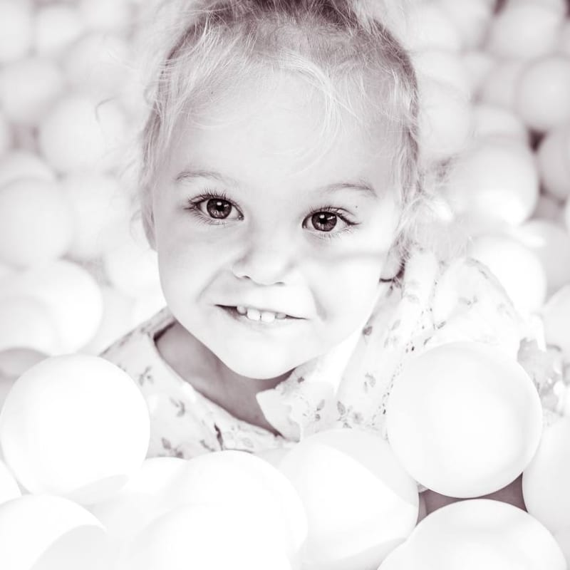 Anya smiling among soft play balls, in soft black and white