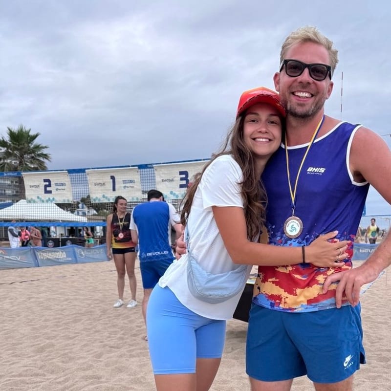 Stas and Masha hugging on the beach after a volleyball match, a medal around his neck