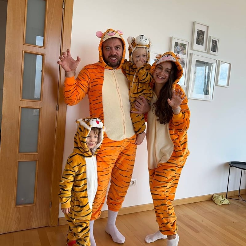 The whole family together at home in matching tiger onesies, waving