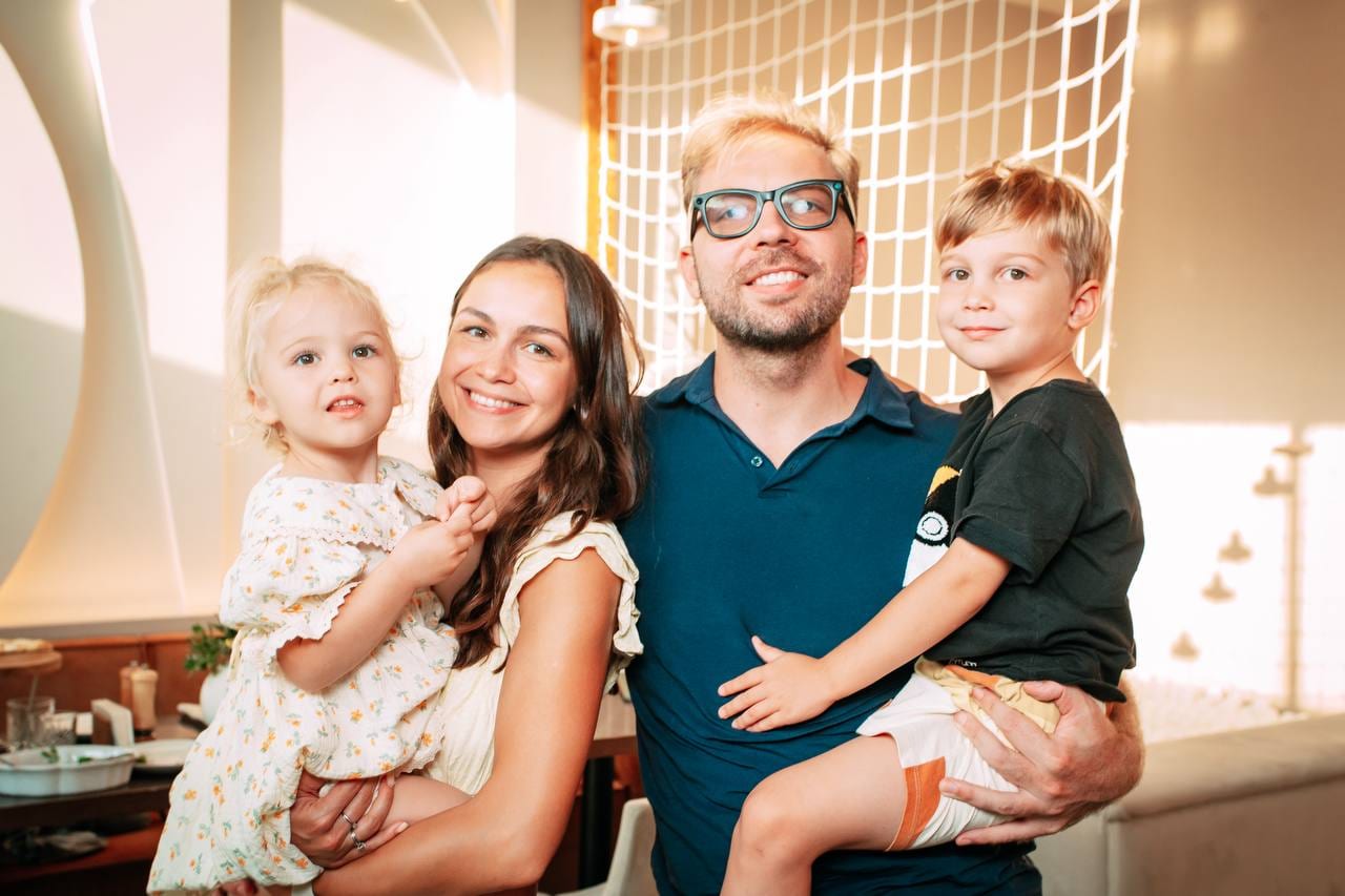 Stas and Masha holding their two children, all smiling at a café